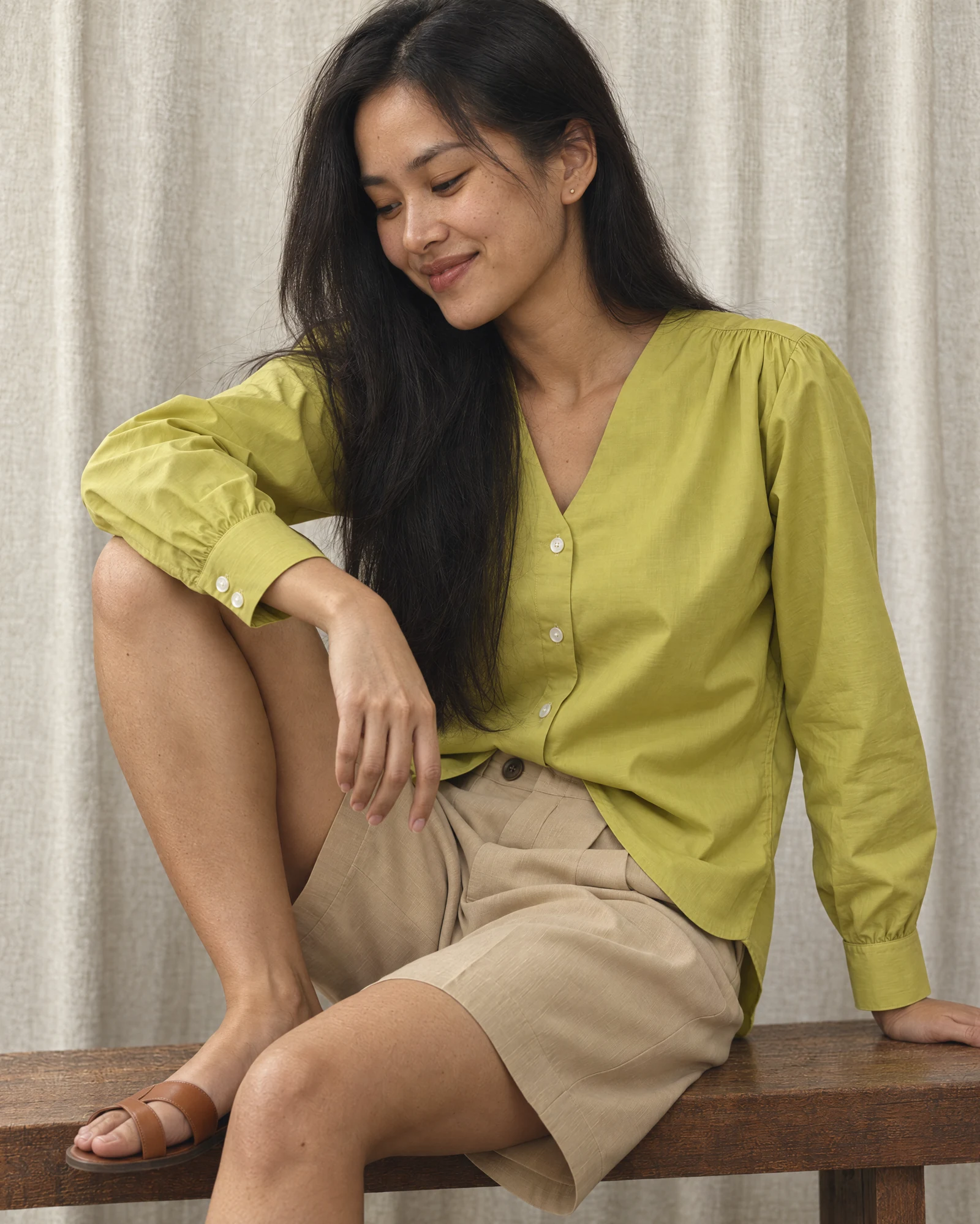 Perempuan memakai Lime Kiya Poplin Shirt dan Cream Short Lily Prime Pant, duduk di bangku kayu